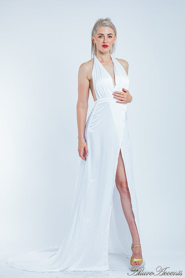 Woman wearing a white silk satin, halter neck gown with a high leg slit.