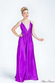 Woman wearing a plum purple long satin dress that has a deep v neckline.