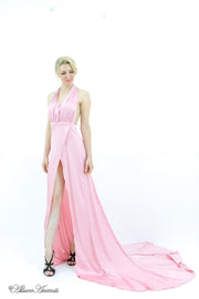 Woman wearing a baby pink silk satin, halter neck gown with a high leg slit.