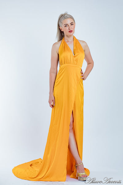 Woman wearing an orange silk satin, halter neck gown with a high leg slit.
