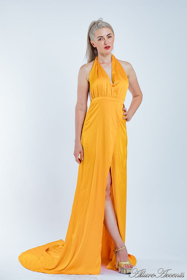 Woman wearing an orange silk satin, halter neck gown with a high leg slit.