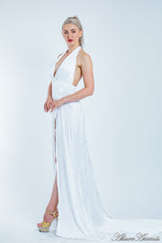 Woman wearing a white silk satin, halter neck gown with a high leg slit.