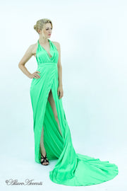 Woman wearing a lime green silk satin, halter neck gown with a high leg slit.