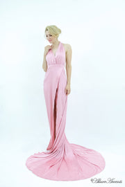 Woman wearing a baby pink silk satin, halter neck gown with a high leg slit.